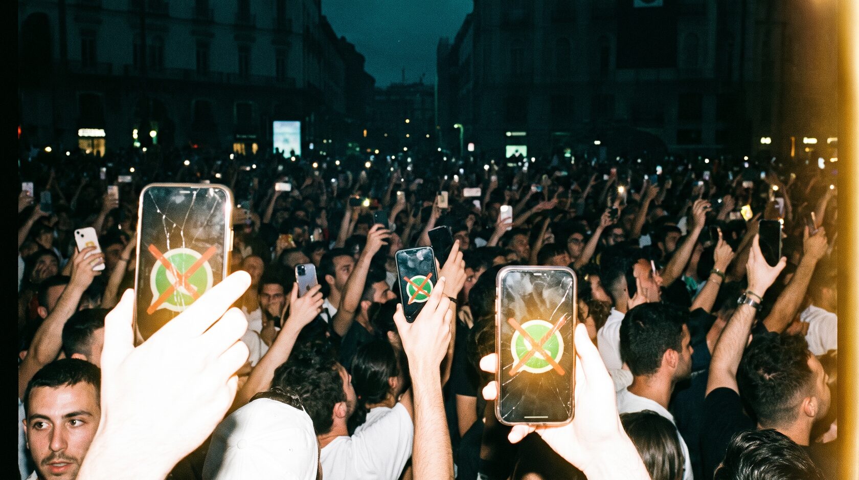A crowd raising phones showing a crossed-out WhatsApp logo.