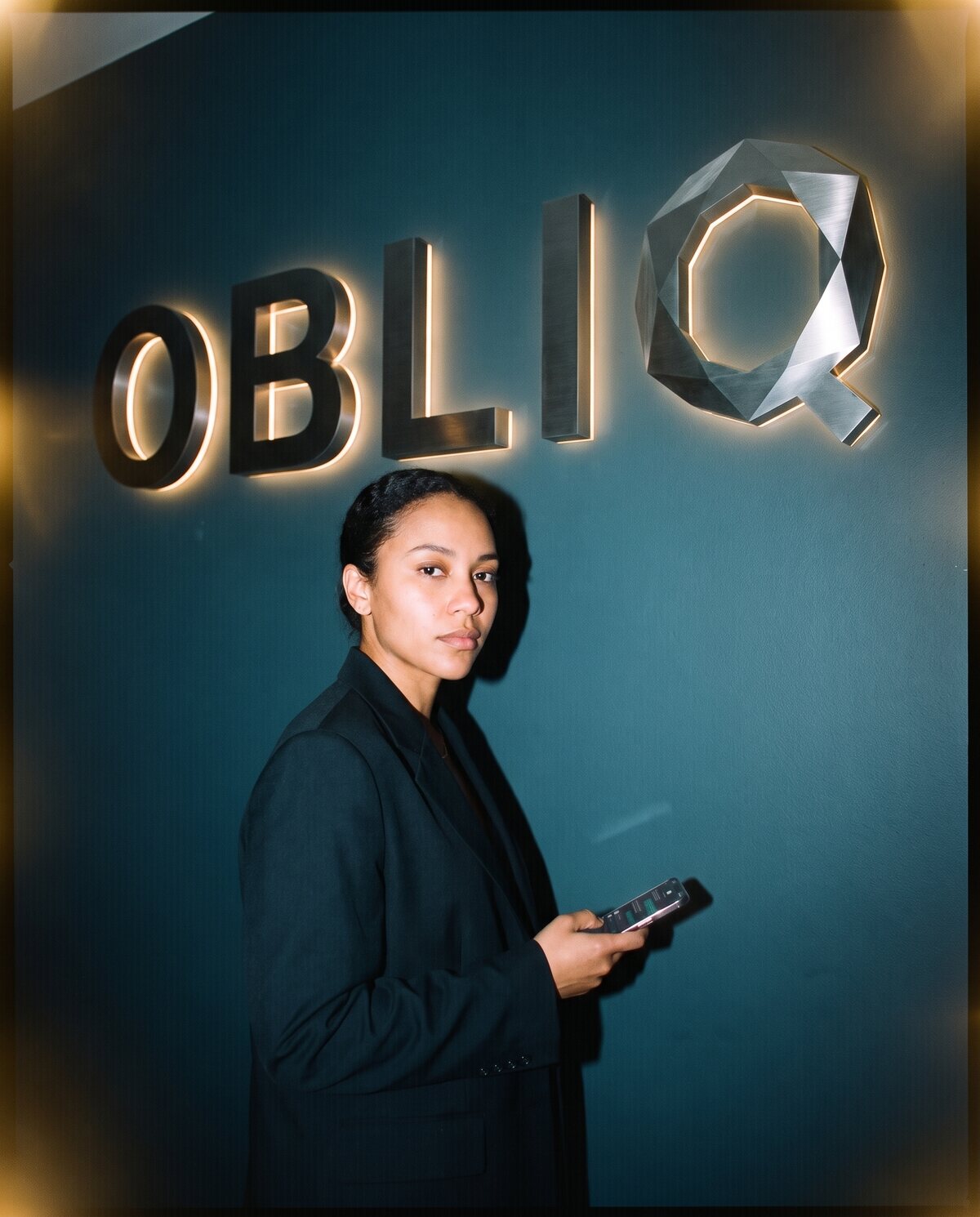 A composed person holding their phone in a dark room, quietly in control of their own messaging.